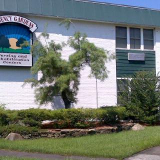 A white school building with a green and blue sign, surrounded by greenery.