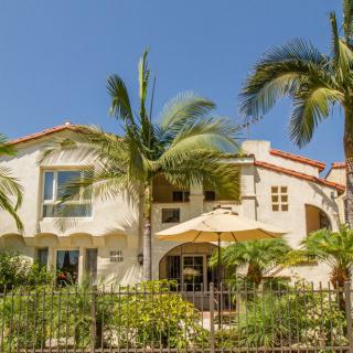 A beautiful tropical-style house surrounded by palm trees and a well-maintained garden on a sunny day.