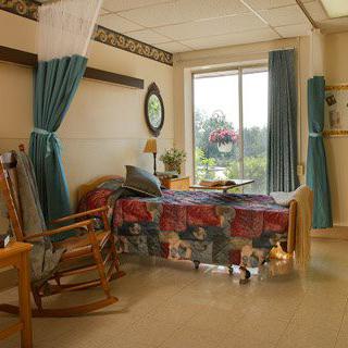 A cozy hospital room with a bed, rocking chair, and a large window letting in natural light.