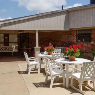 A sunny patio area with white tables and chairs, adorned with potted red flowers.