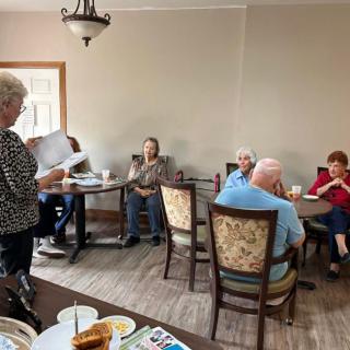 A group of seniors gathered in a room, socializing and having a meeting around tables.