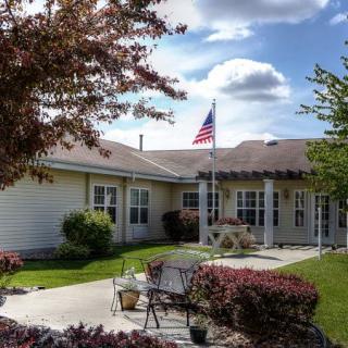 A cozy residential home with a patio and garden, featuring an American flag under a partly cloudy sky.