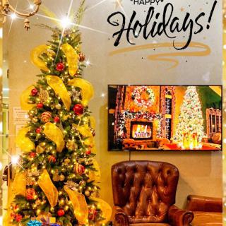 A festive holiday display featuring a beautifully decorated Christmas tree with yellow ribbons and ornaments, accompanied by a cozy chair and an image of a fireplace.