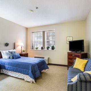 A cozy bedroom with blue bedding, a television, and a window letting in natural light.