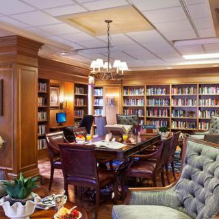 A cozy library room with wooden furniture and bookshelves filled with books, offering comfortable seating and a warm lighting ambiance.