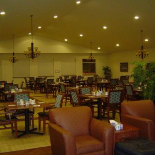 A spacious restaurant interior with arranged tables, chairs, and comfortable seating under warm lighting.