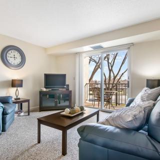A cozy living room featuring comfortable couches, a television, and a coffee table, with a view of the balcony through glass doors.
