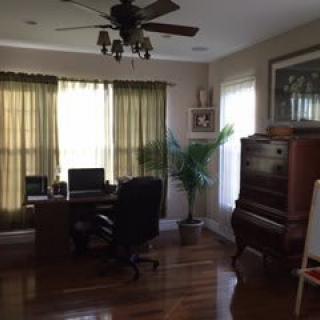 A cozy home office with a desk, computer, and piano by the window.