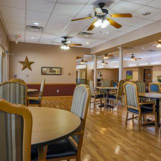 A spacious and well-lit dining area with tables and chairs, featuring ceiling fans and wooden flooring.
