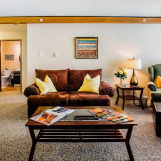 A cozy living room featuring a brown sofa, green armchair, and wooden coffee table with magazines.
