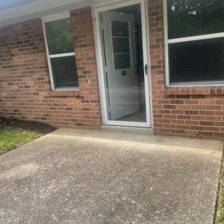 A small patio area with a glass door and windows on a brick wall.