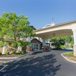 A welcoming hotel entrance with a covered driveway and surrounding greenery under a clear blue sky.