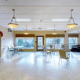 A spacious room with chairs and tables, featuring large windows and overhead lighting.