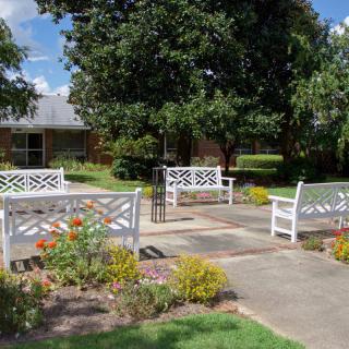A peaceful garden scene with white benches, colorful flowers, and lush trees.
