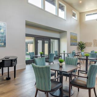 A modern dining area with large windows, stylish chairs and tables, complemented by a grand piano and decorative plants.