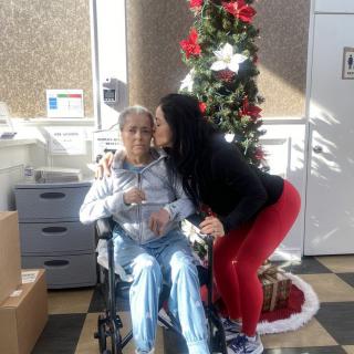 A warm family moment during the Christmas holiday, with an elderly person in a wheelchair receiving a kiss.