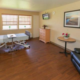 A clean and well-furnished hospital room with a bed, television, and flowers on a table.