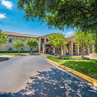 A sunny view of a hotel entrance surrounded by trees and a well-maintained driveway.