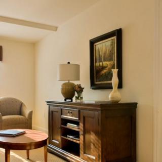 A cozy living room with elegant decor, featuring a wooden cabinet, lamp, and artwork on the wall.