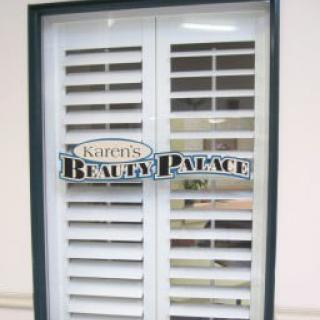 A window with white shutters and a 'Kathy's Beauty Palace' sign.