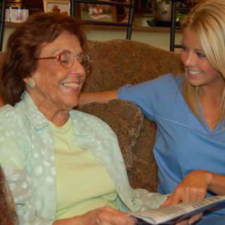 An elderly person and a caregiver sharing a happy moment while looking at a book together.