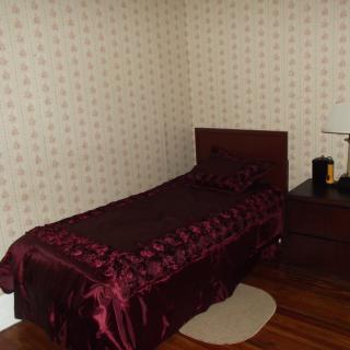 A small bedroom with a single bed, patterned wallpaper, and a wooden nightstand with a lamp.