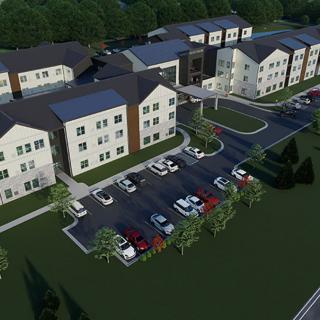 An aerial view of a modern housing complex with multiple buildings and a parking lot surrounded by landscaped greenery.