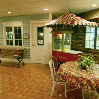 An indoor area featuring a popcorn machine with a striped canopy, a table covered with a colorful tablecloth, and seating options including a bench.