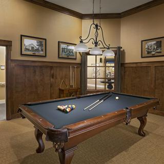 A well-lit billiard room featuring a classic pool table with wooden legs and a hanging chandelier.