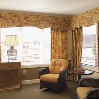 A cozy living room with patterned curtains, an armchair, and a lamp by the window.