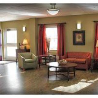 A cozy living room with a sofa, armchair, and coffee table, decorated with red curtains and wall art.