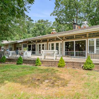 A spacious house surrounded by greenery, featuring a large deck and well-maintained lawn.