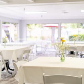 A bright and airy restaurant dining area with white tablecloth-covered tables and floral centerpieces.
