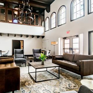 A spacious and elegantly designed living room features modern furniture, a high ceiling, and large arched windows.