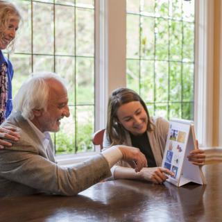 A joyous family gathering as a younger woman shares a photo album with two seniors at a table near a window.