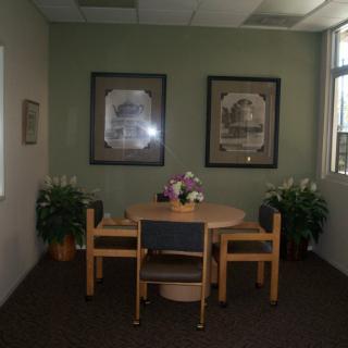 A small meeting room with a round table and four chairs, adorned with plants and framed artwork on the walls.