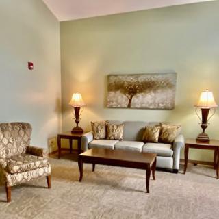 A cozy living room with a sofa, armchair, coffee table, and two lamps flanking a large piece of wall art.