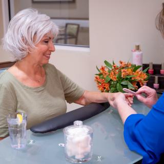 A senior woman receiving a manicure at a nail salon.