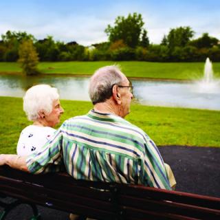 An elderly couple sitting on a bench by a lake, enjoying the serene park view.