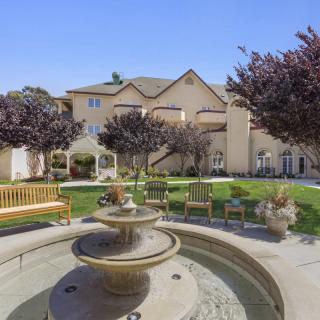 A peaceful courtyard with a fountain, surrounded by benches and landscaping in front of a building.