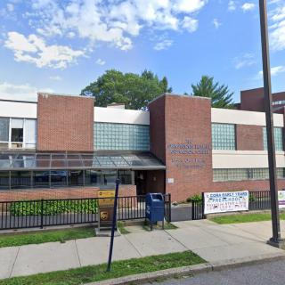 A brick building with a fence and sidewalk in an urban setting, possibly a school.