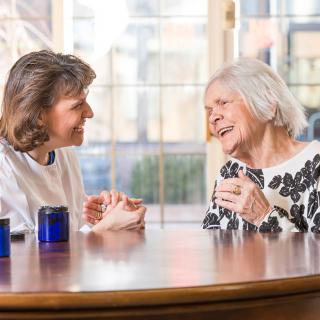 A caregiver and an elderly woman enjoying a conversation over coffee.