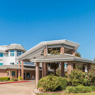 A modern residential building with a prominent entrance and landscaped surroundings under a clear blue sky.