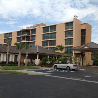 A multi-story hotel with palm trees and a car parked in the lot.
