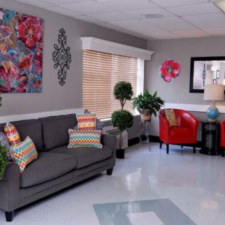 A cozy living room with a gray couch, red armchairs, colorful pillows, and decorative artwork.