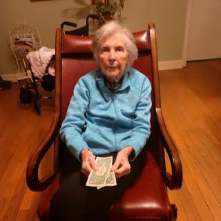 An elderly woman sitting in a rocking chair, holding two bills.