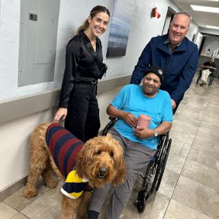 A heartwarming moment featuring a friendly dog visiting a patient in a hospital, accompanied by two supportive individuals.