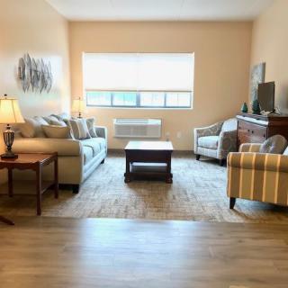 A cozy living room with a sofa, armchairs, and a coffee table, featuring a television and a window letting in natural light.