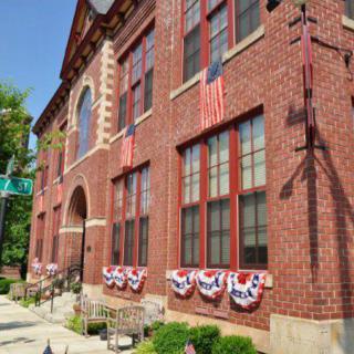 A historic brick building adorned with American flags and patriotic decorations along a sidewalk.