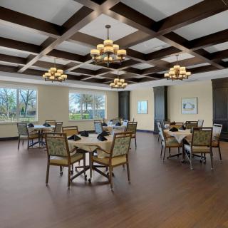 A spacious dining room with elegant chandeliers, wooden flooring, and beautifully arranged tables and chairs.